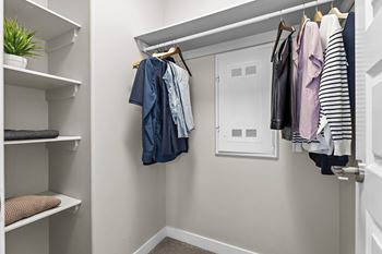 A white closet with clothes hanging and shelves with items.